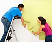 Attractive young adult couple painting interior wall of house.