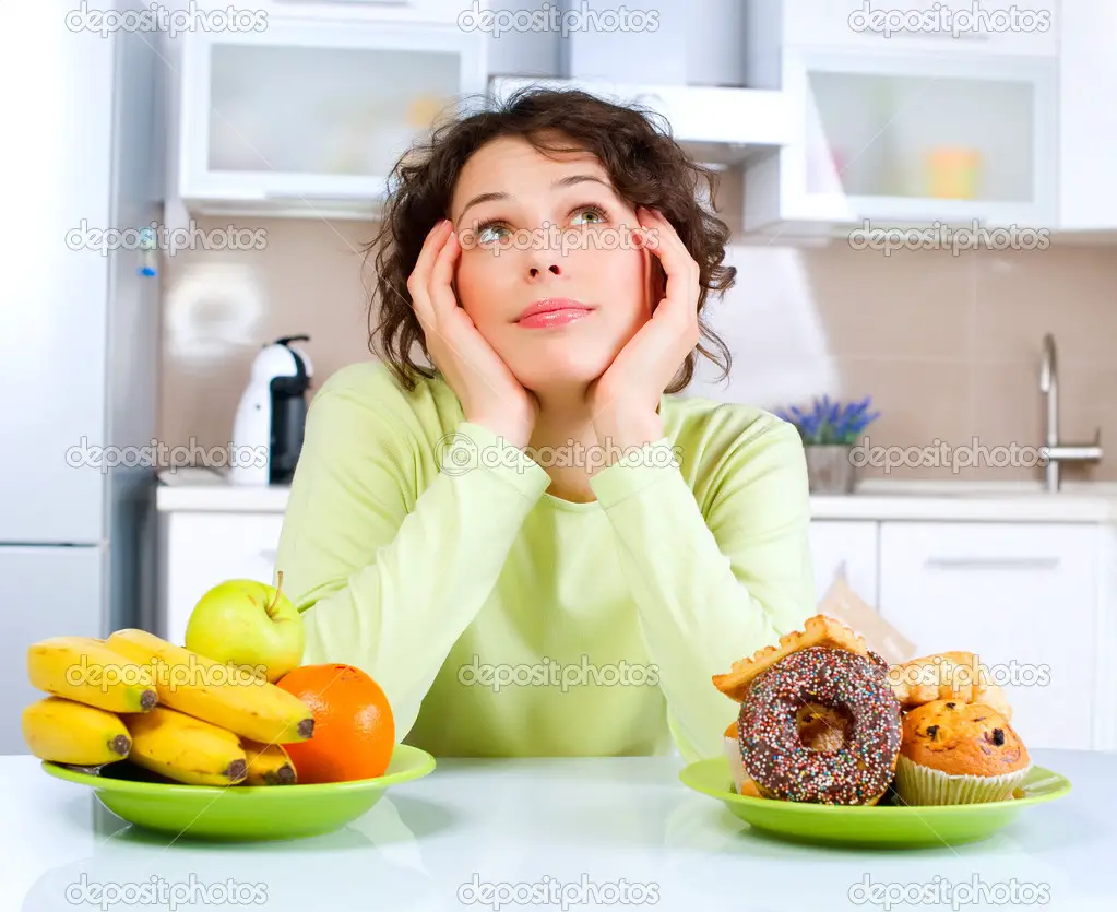 Beautiful Young Woman choosing between Fruits and Sweets